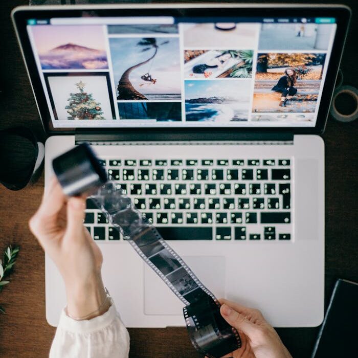 Person holding film strip over laptop showcasing photography work.